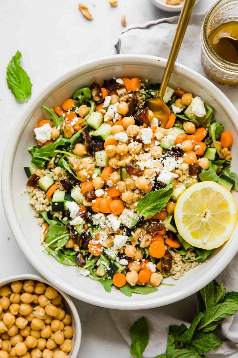 A top shot of a large bowl of carrot chickpea salad with feta cheese and a slice of lemon.