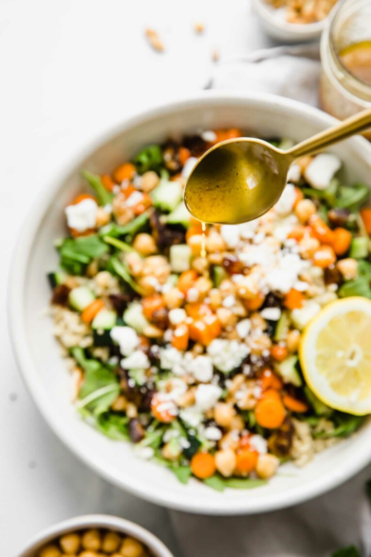 A spoon of carrot salad dressing dripping over the carrot salad.