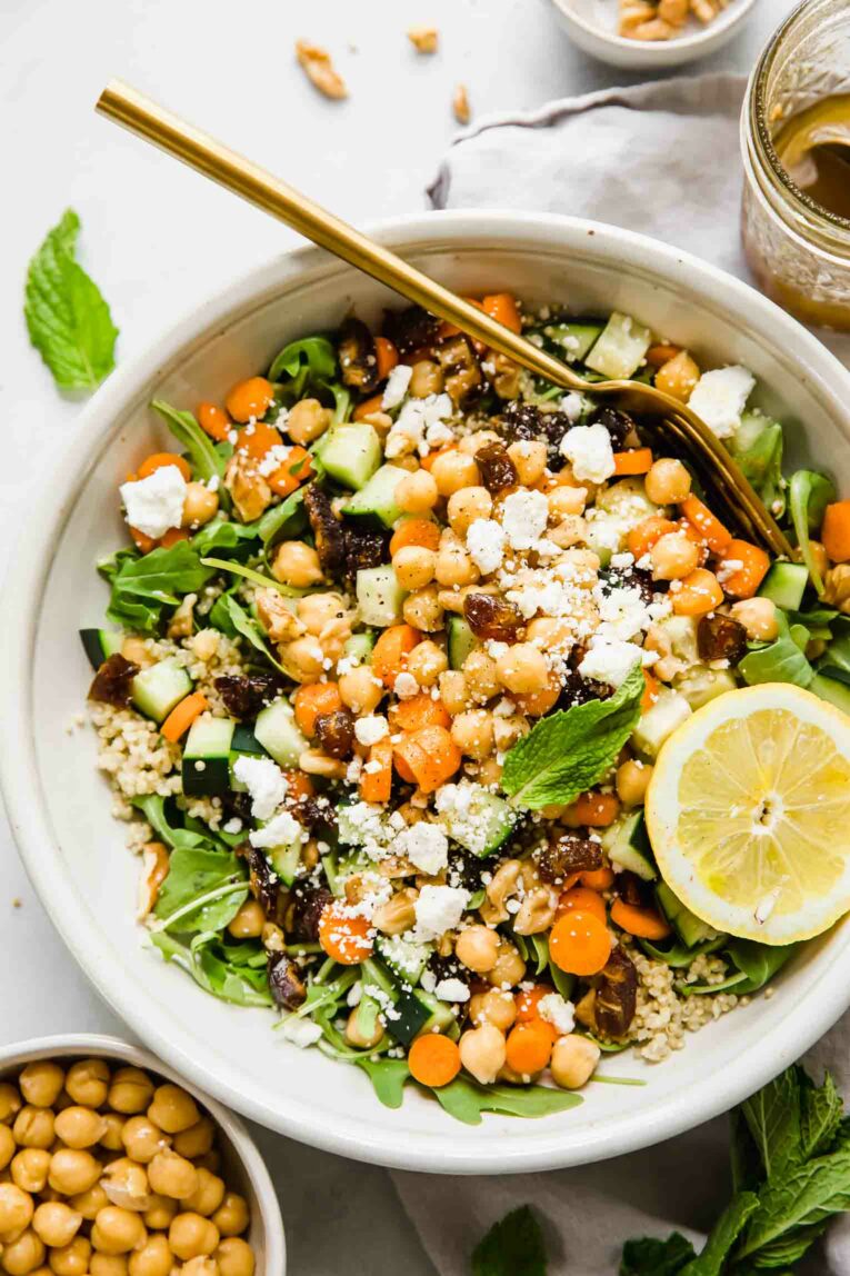 A top shot of a large bowl of carrot chickpea salad with feta cheese and a slice of lemon.