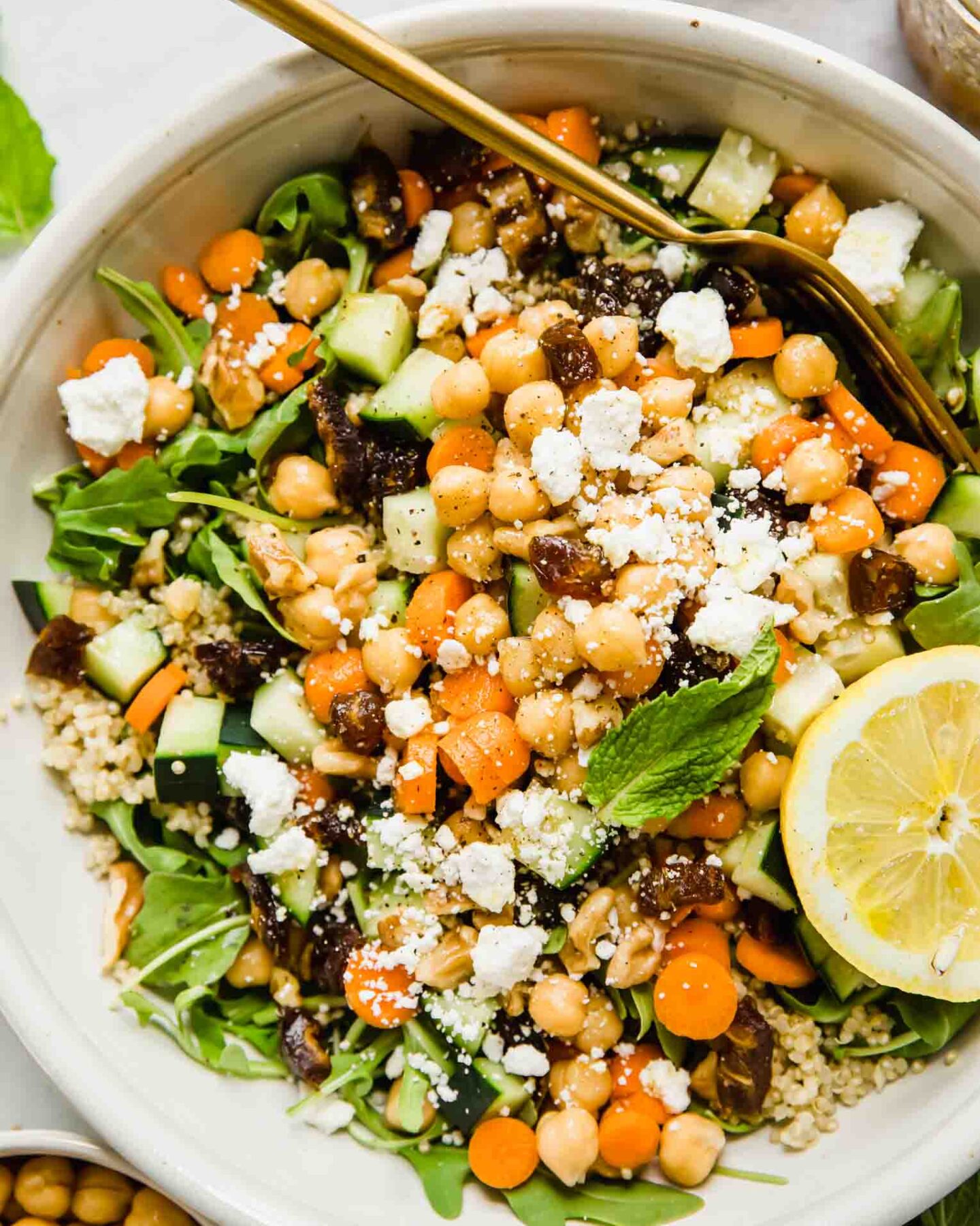 A top shot of a large bowl of carrot chickpea salad with feta cheese and a slice of lemon with a gold fork.