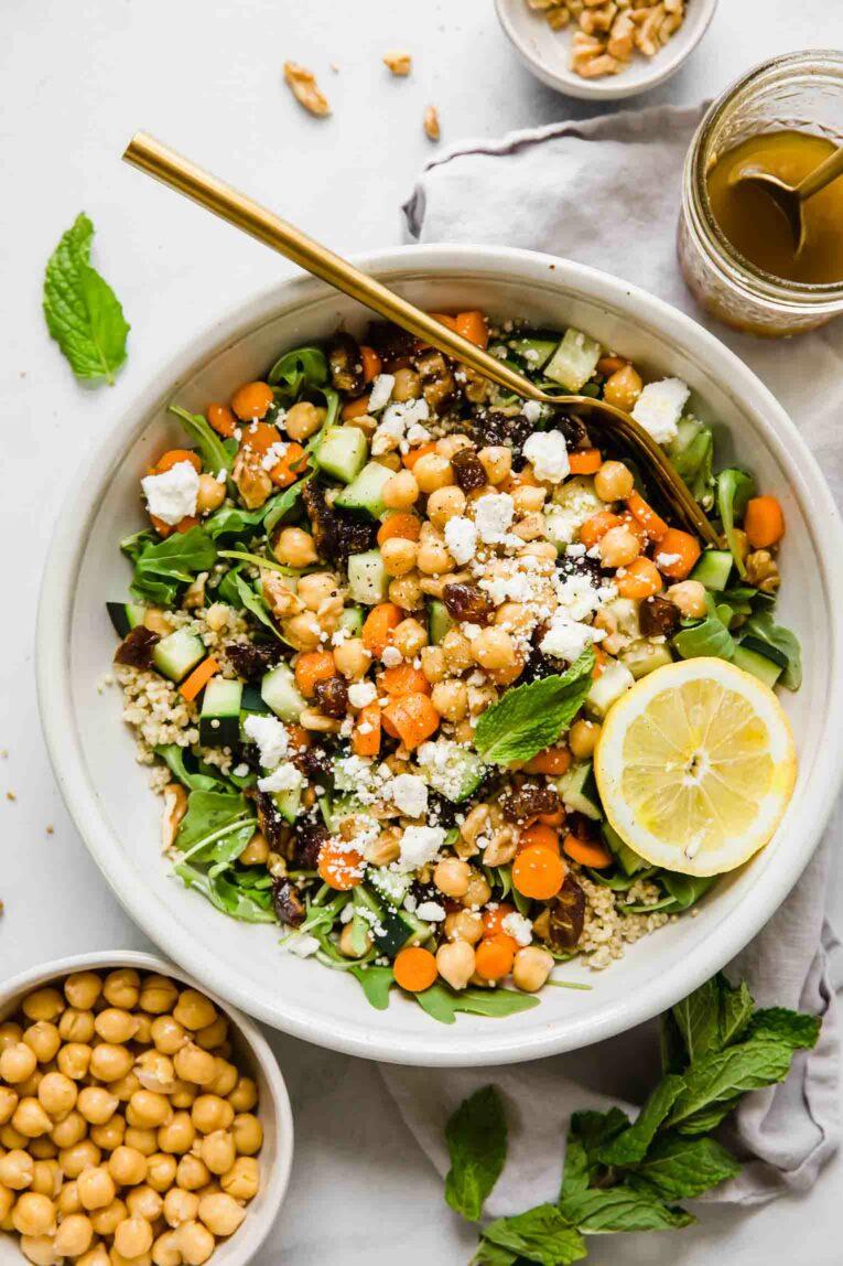 A top shot of a large bowl of carrot chickpea salad with feta cheese and a slice of lemon with a bowl of chickpeas to the side.