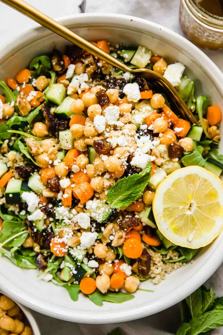 A top shot of a large bowl of carrot chickpea salad with feta cheese and a slice of lemon.