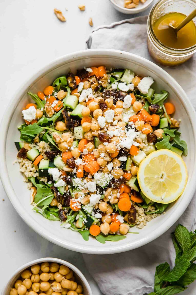 A top shot of a large bowl of carrot chickpea salad with feta cheese and a slice of lemon.