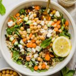 A landscape view of a large bowl of carrot chickpea salad with feta cheese and a slice of lemon.