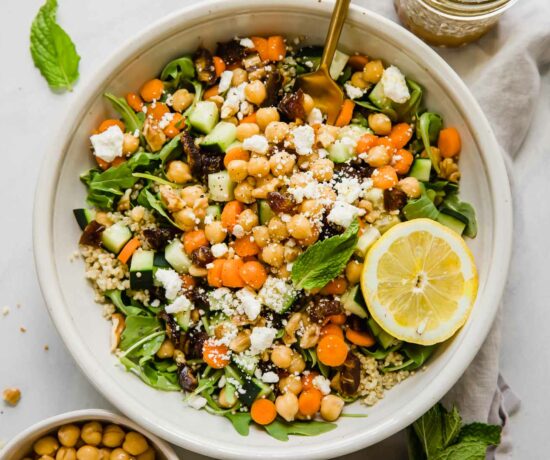 A landscape view of a large bowl of carrot chickpea salad with feta cheese and a slice of lemon.