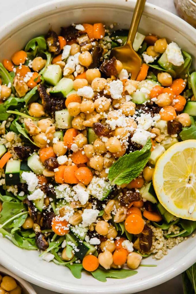A landscape view of a large bowl of carrot chickpea salad with feta cheese and a slice of lemon.