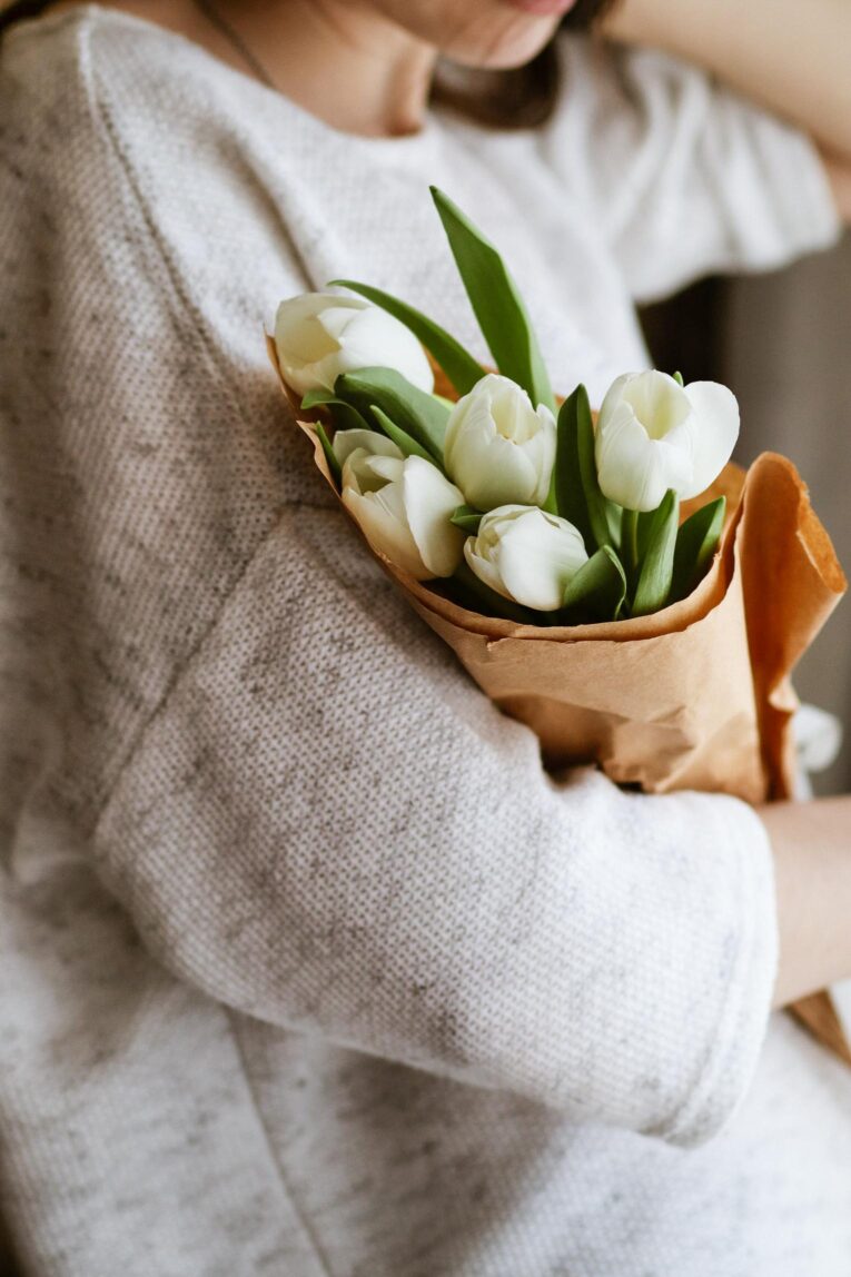 Mother in a white sweater holding flowers.
