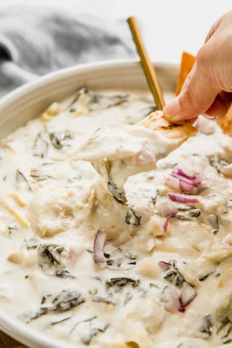 Angled shot of chip dipping into slow cooker spinach artichoke dip.