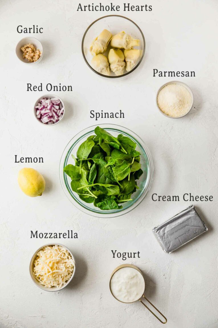 Ingredients for Slow Cooker Spinach Artichoke Dip on a white table.