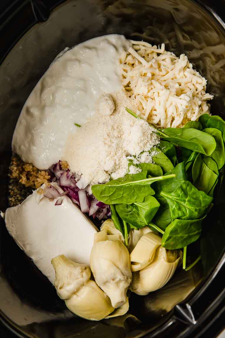 Ingredients for spinach artichoke dip in a slow cooker.