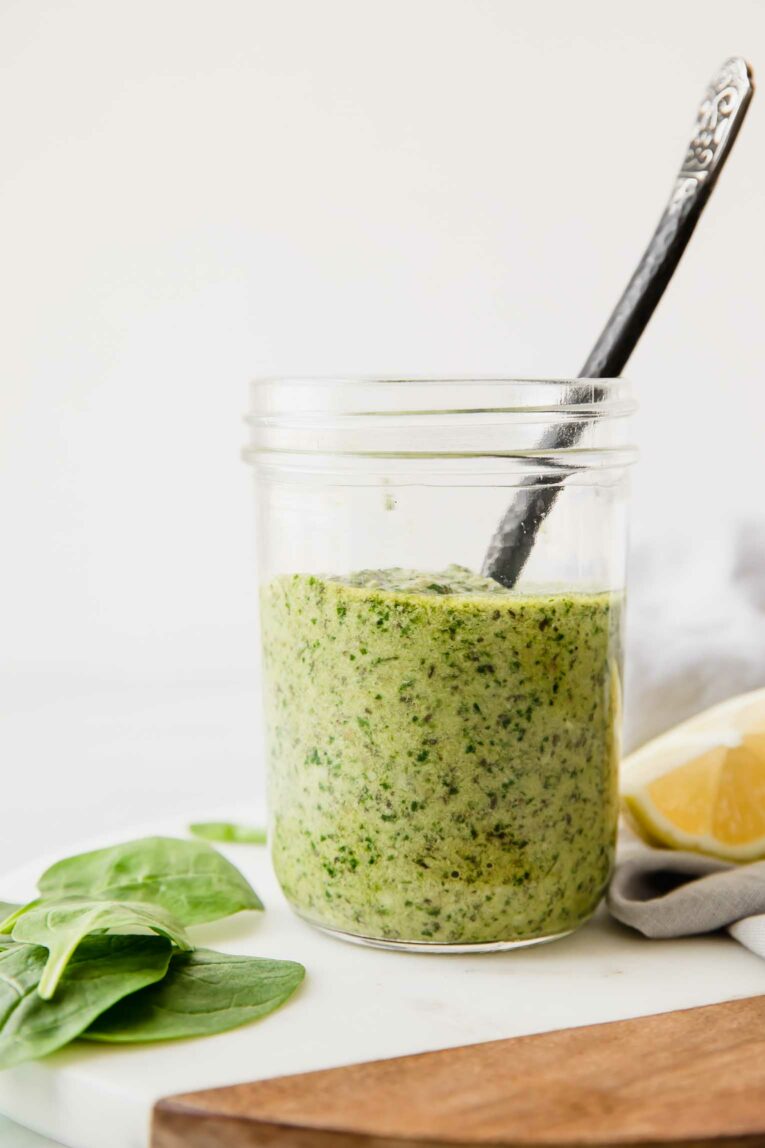 A mason jar full of spinach pesto sauce with a spoon coming out of the jar.