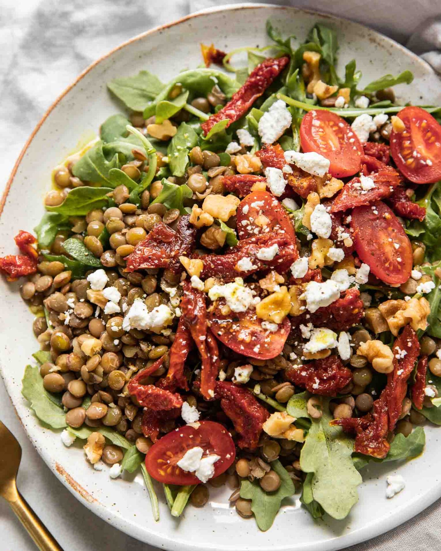 Close up of lentil arugula salad topped with sun-dried tomatoes and goat cheese.
