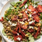 Close up of lentil arugula salad topped with sun-dried tomatoes and goat cheese.
