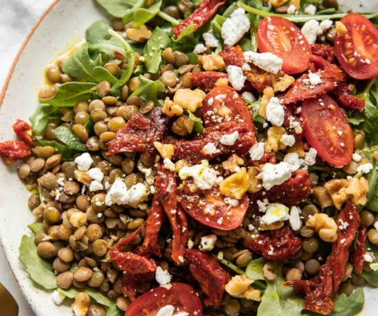 Close up of lentil arugula salad topped with sun-dried tomatoes and goat cheese.