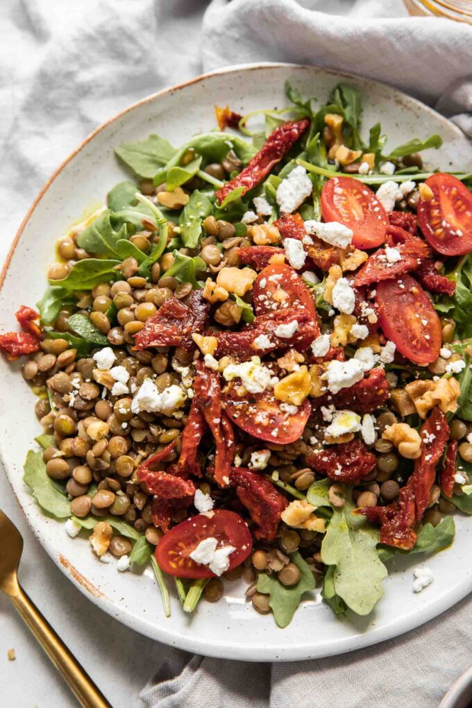 Close up of lentil arugula salad topped with sun-dried tomatoes and goat cheese.