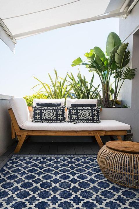An outdoor rug with a bench on top on a deck.