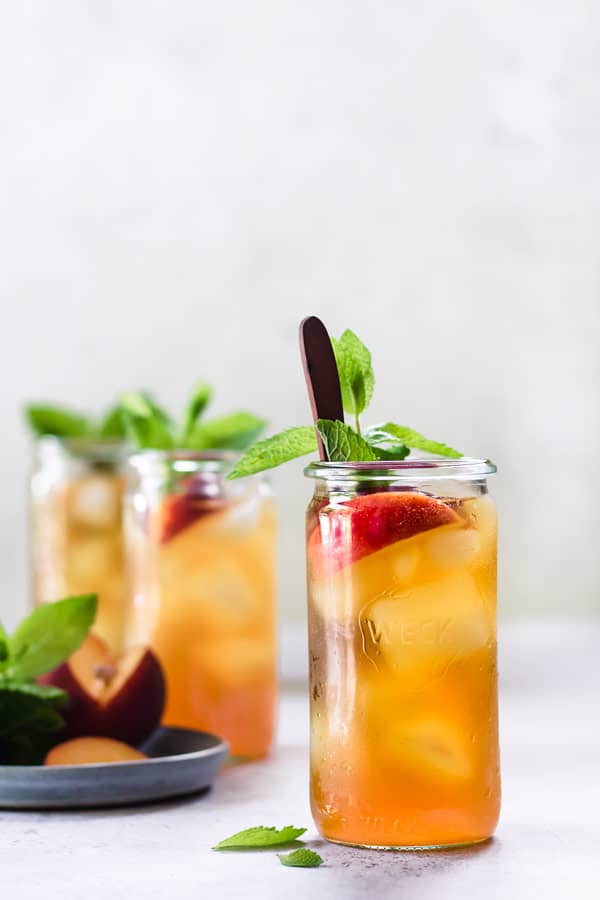 Three glasses of cold brew peach iced tea with min leaves and peaches inside. 
