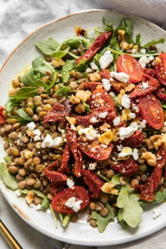 Close up of lentil arugula salad topped with sun-dried tomatoes and goat cheese.