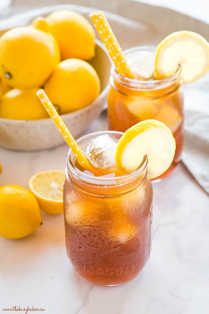 A mason jar with iced tea and a yellow straw with lemon wedges.
