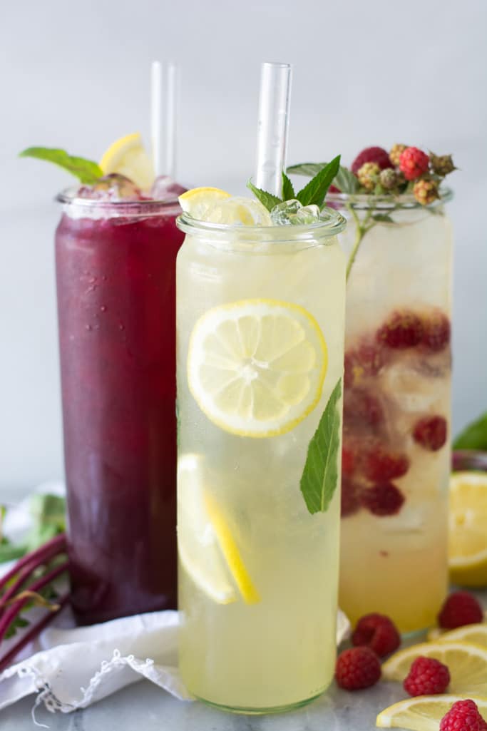 Three jars with lemonade and fruit cut up inside.