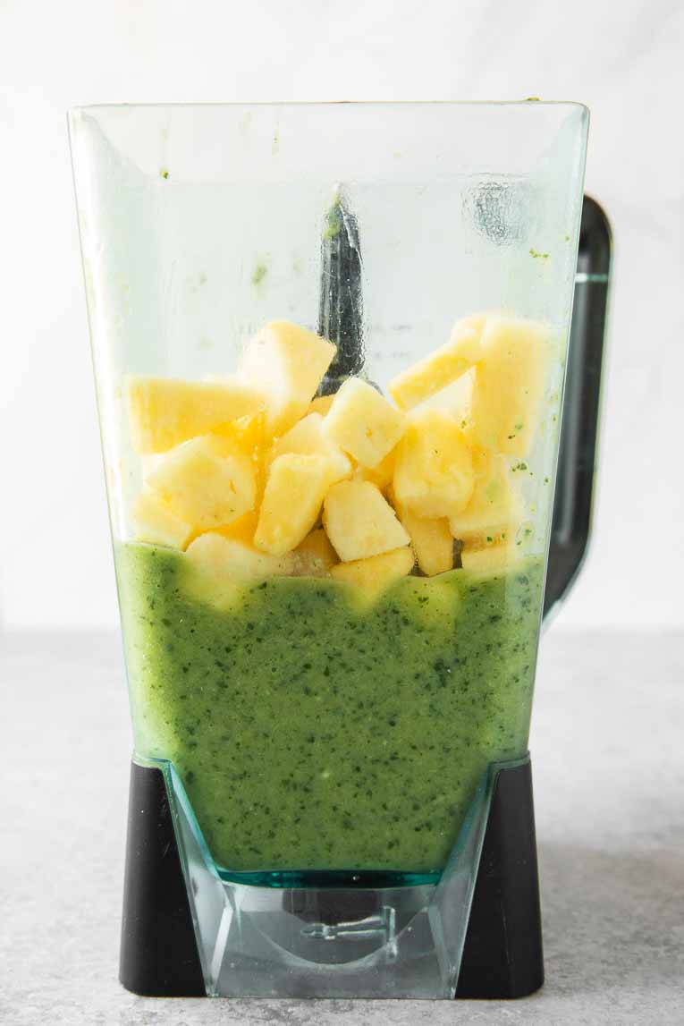 Green detox smoothie with pineapple chunks in a blender.