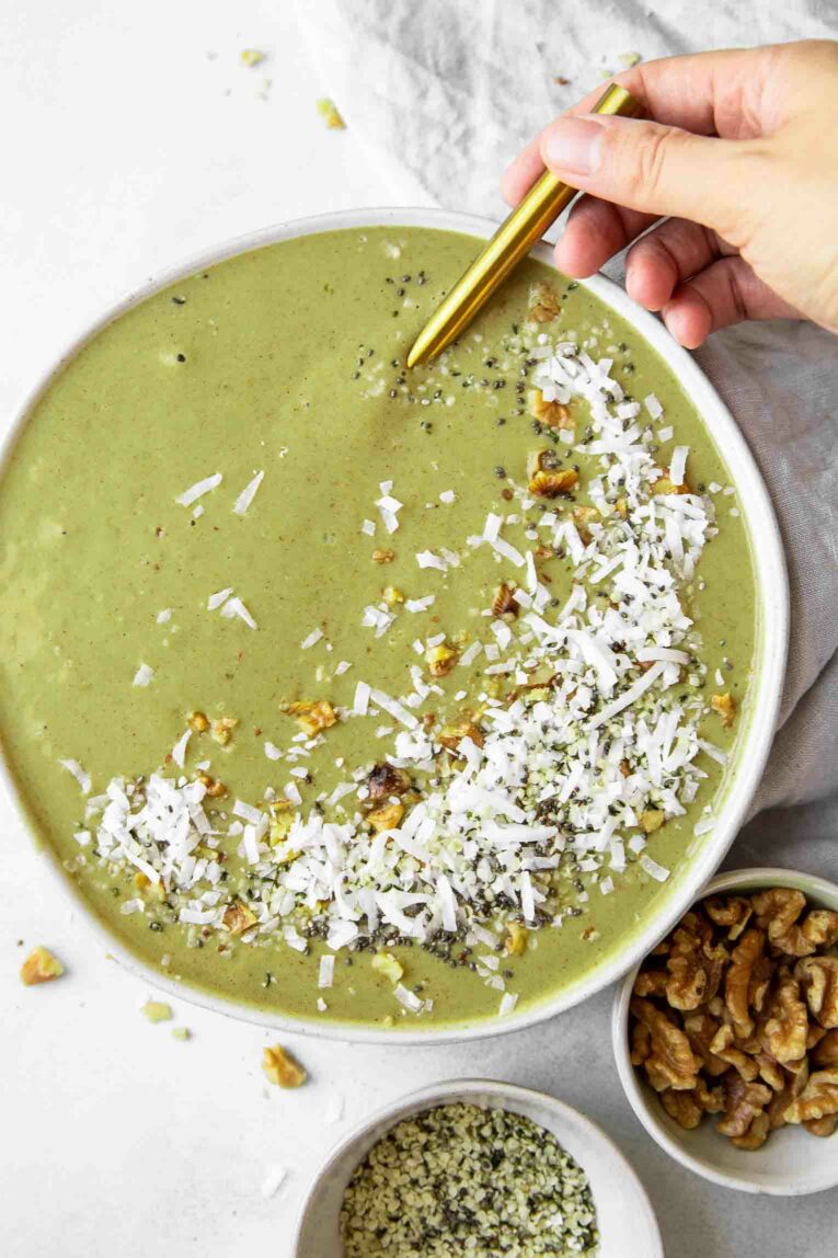 Hand holding spoon in matcha smoothie bowl.