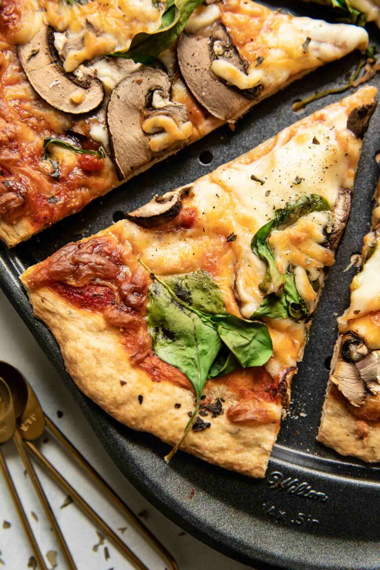 Slice of vegan pizza topped with red sauce, vegan cheese, spinach, and mushrooms.