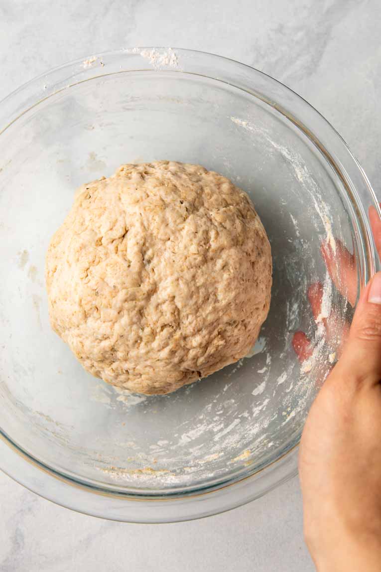 Pizza dough rolled into a ball in a glass bowl.