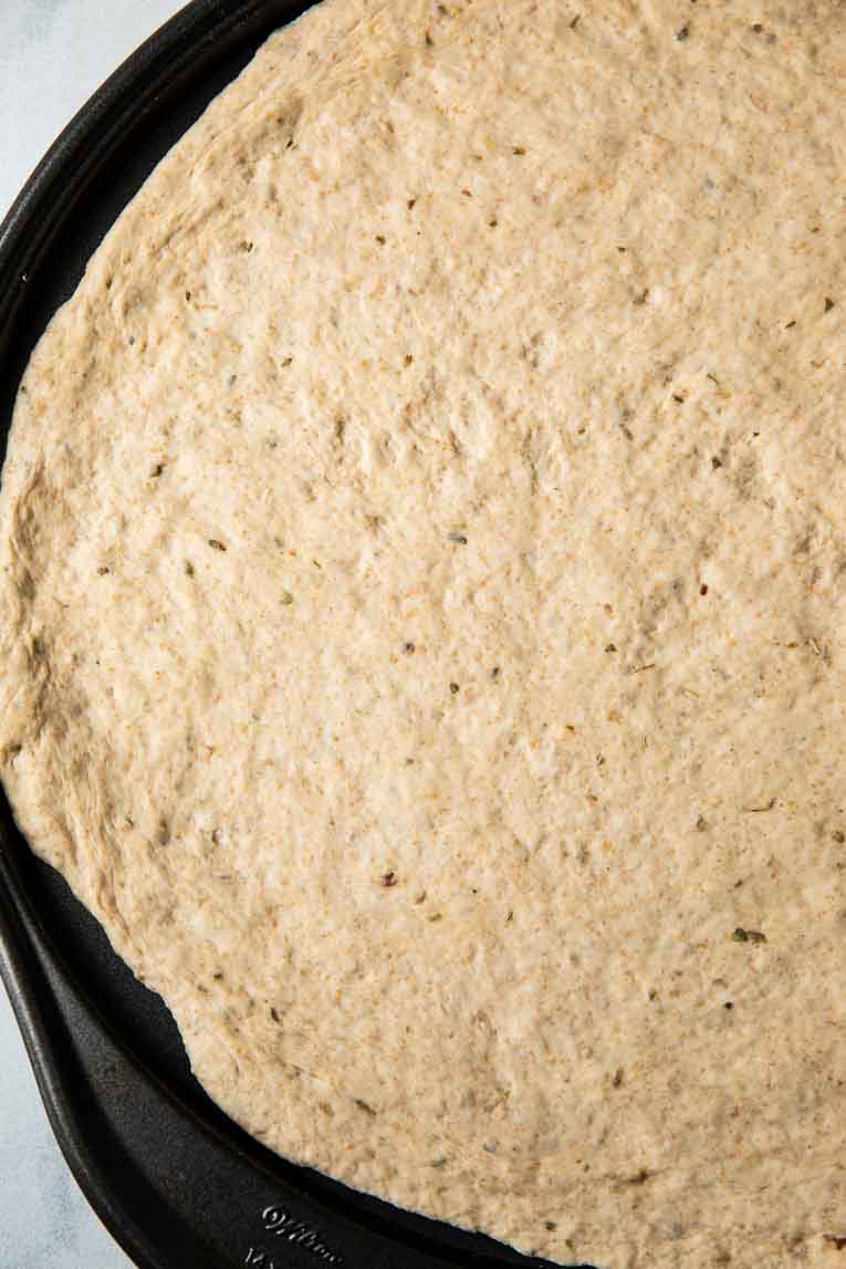 Flattened vegan pizza dough on a baking pan.