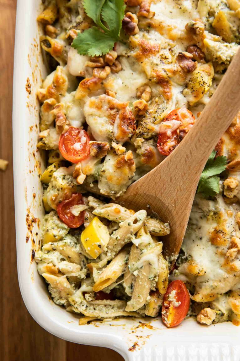 Close up of wooden spoon scooping Chicken Pesto Pasta Bake out of casserole dish.