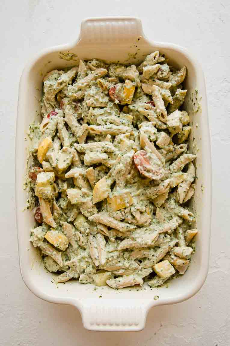 Pesto pasta, tomatoes, chicken, and summer squash in a casserole dish.