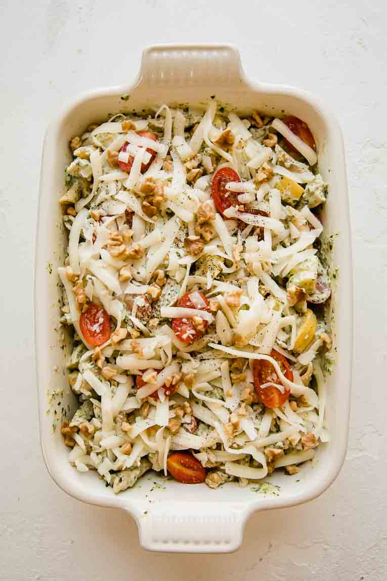 Pesto pasta with chicken and vegetables in a casserole dish with mozzarella.