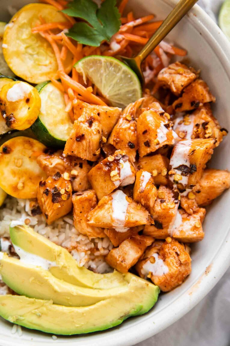 Top shot of bowl of hot honey chicken, rice, zucchini, squash, and avocado with lime.