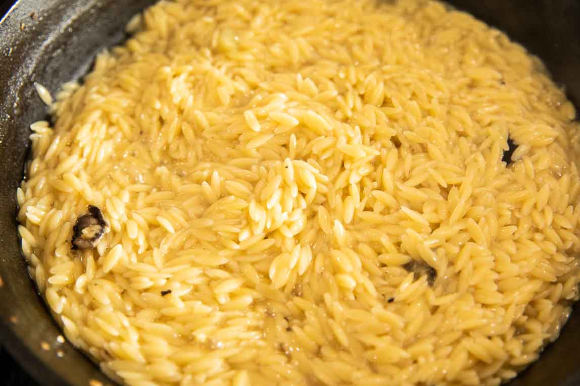 Orzo pasta being cooked in broth in a skillet.