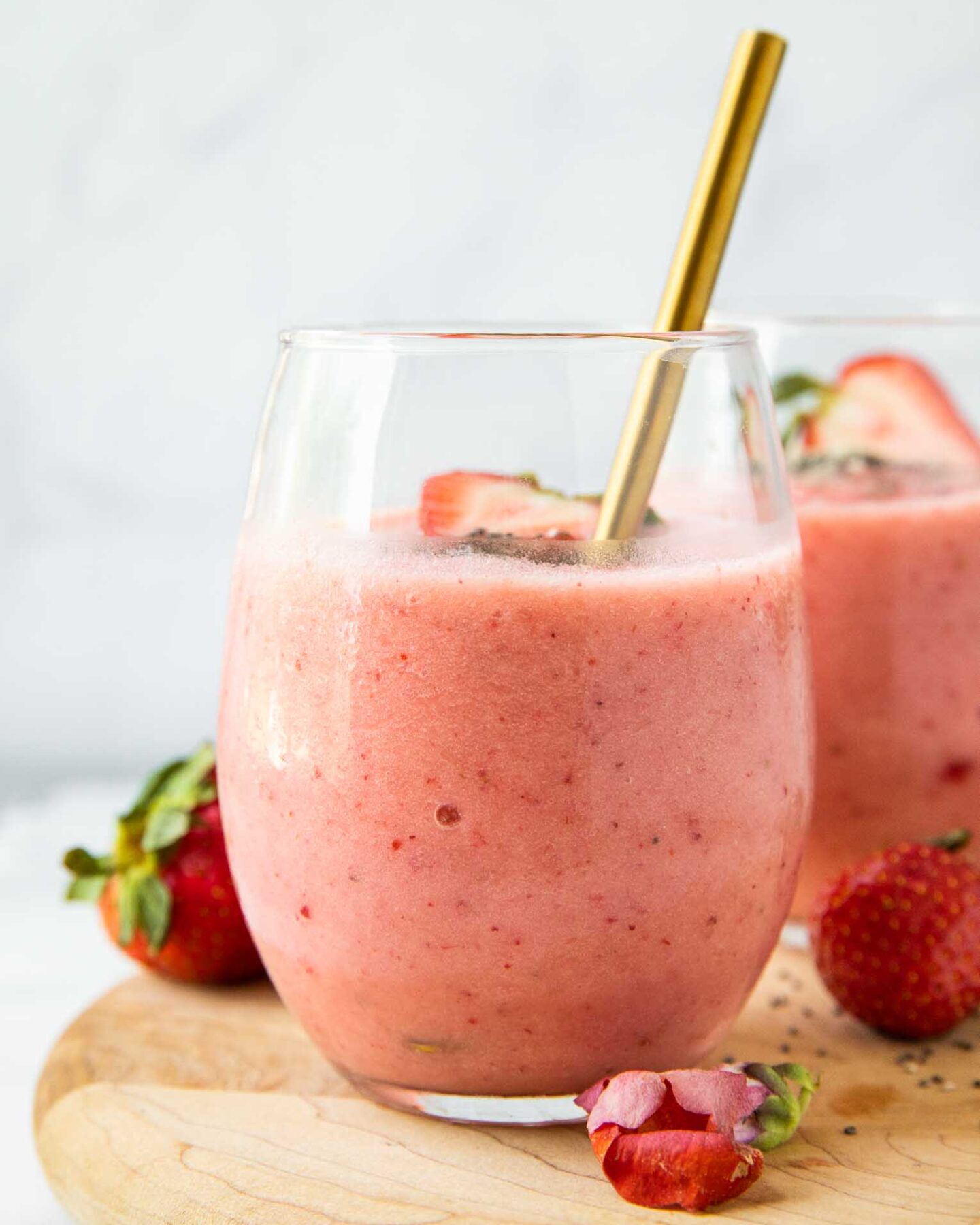 Close up of Strawberry Pineapple Smoothie in a glass cup with fresh strawberries and a spoon.