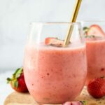 Close up of Strawberry Pineapple Smoothie in a glass cup with fresh strawberries and a spoon.