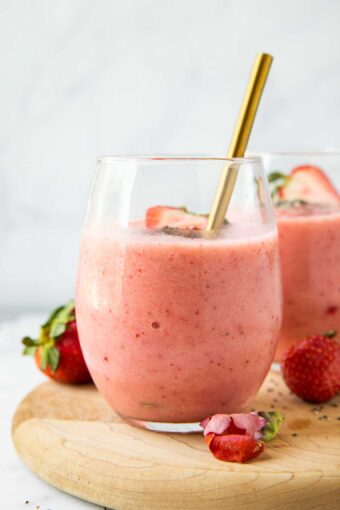 Close up of Strawberry Pineapple Smoothie in a glass cup with fresh strawberries and a spoon.