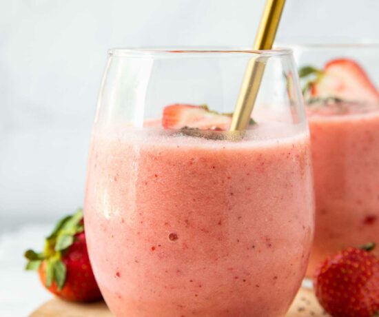 Close up of Strawberry Pineapple Smoothie in a glass cup with fresh strawberries and a spoon.