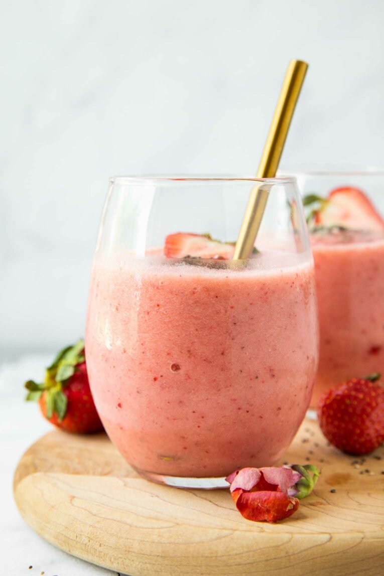 Close up of Strawberry Pineapple Smoothie in a glass cup with fresh strawberries and a spoon.