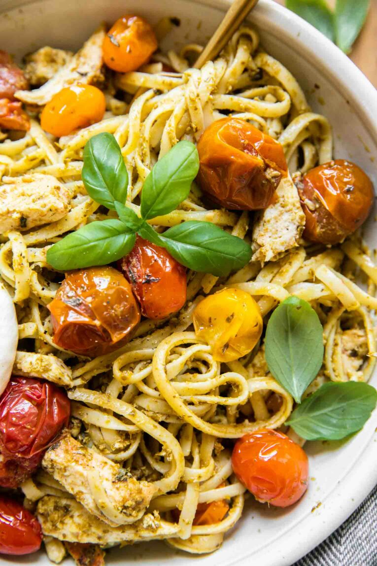 Close up of pesto pasta burrata topped with tomatoes and basil.
