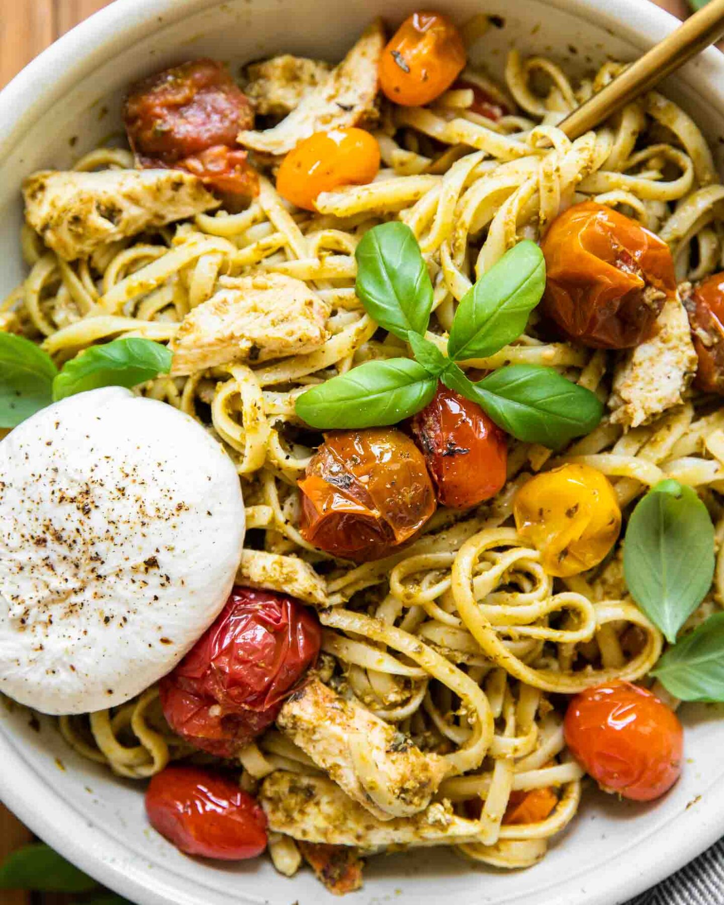 Top shot of Chicken Tomato Pesto Burrata Pasta in a white bowl with a fork.
