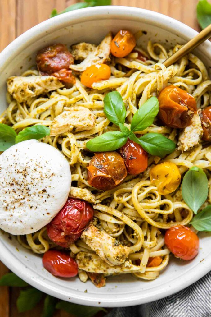 Top shot of Chicken Tomato Pesto Burrata Pasta in a white bowl with a fork.
