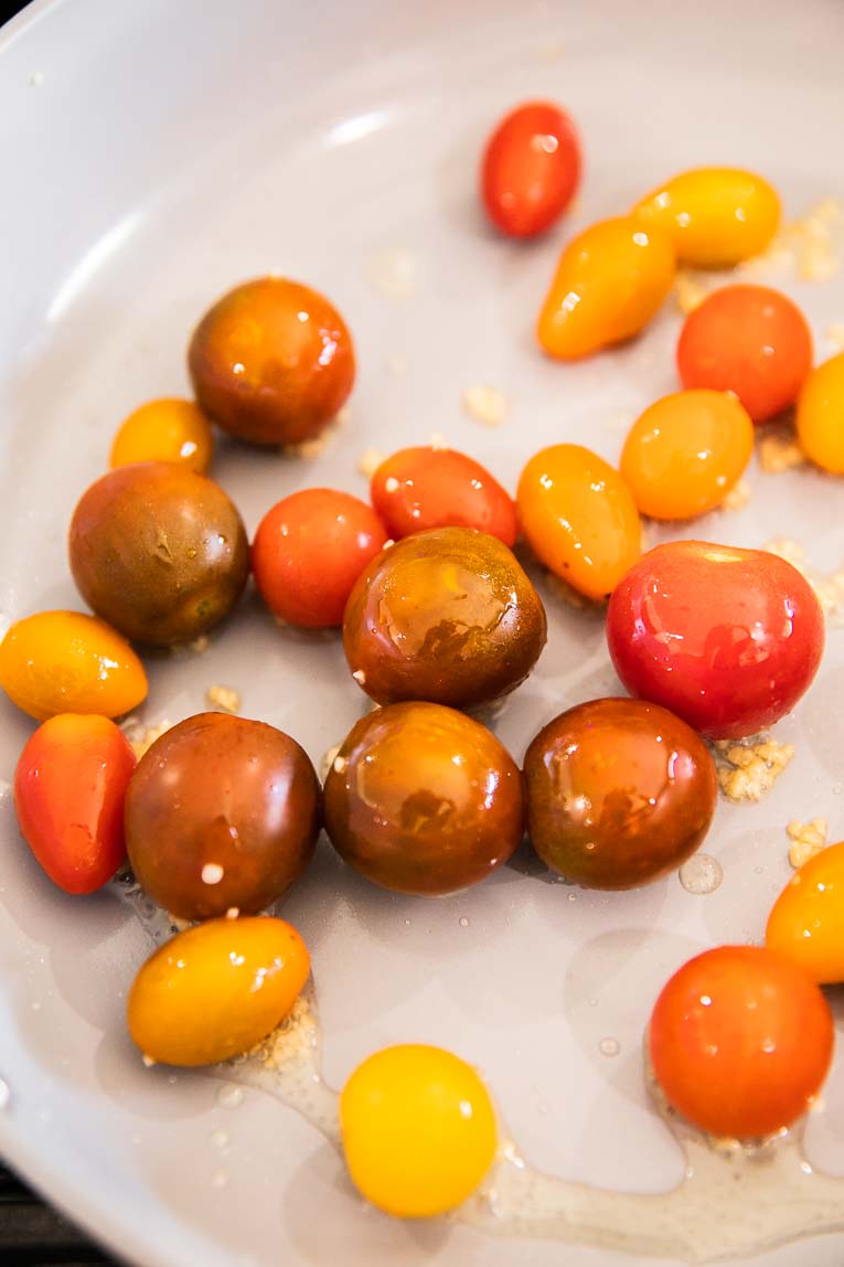 Tomatoes being cooked in a pan with oil and garlic.