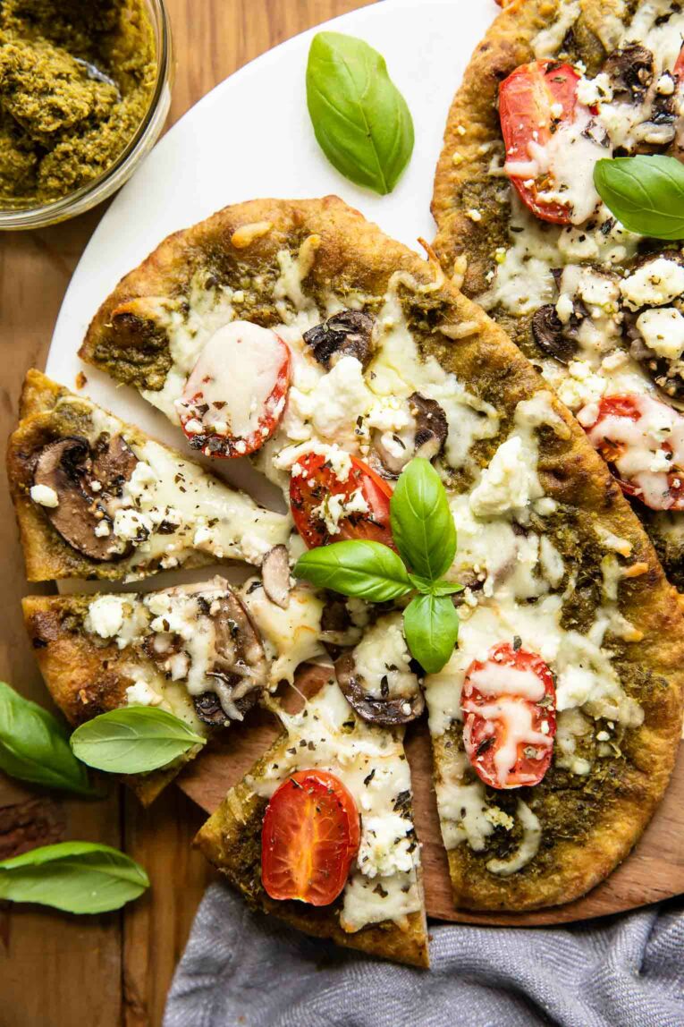 Top shot of goat cheese pizza with spinach pesto, basil, tomatoes, and mushrooms.