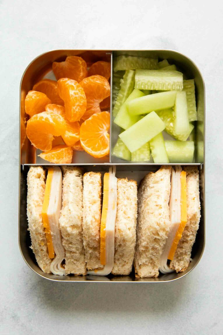 Sandwiches, cucumbers, and oranges for a toddler lunch idea.