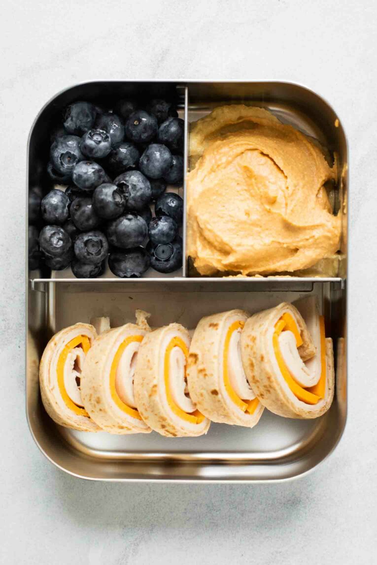 Top shot of toddler bento box with tortilla wrap, hummus, and berries.