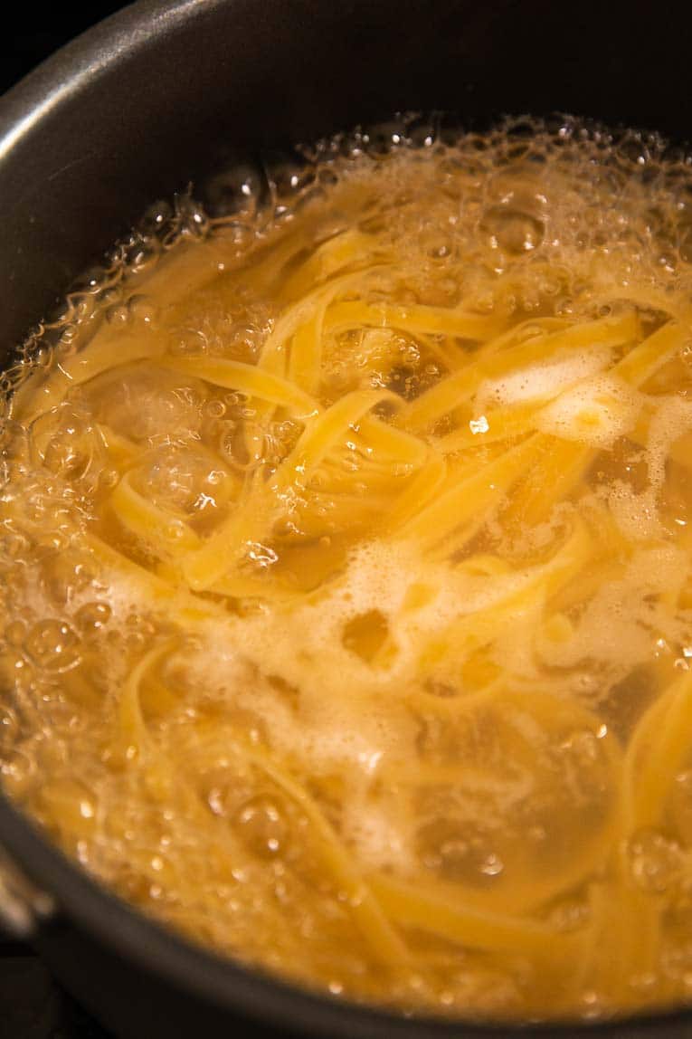 Whole wheat fettuccine being cooked in a pan.