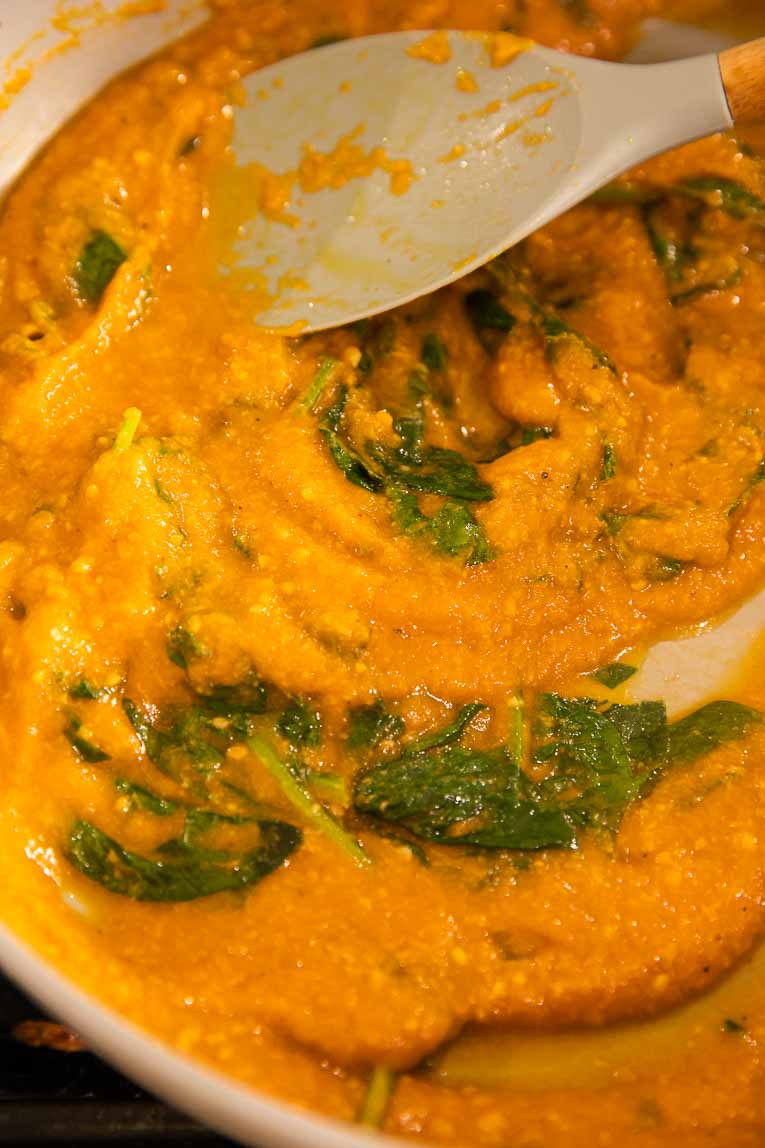 Pumpkin pasta sauce being cooked with spinach in a sauce pan.
