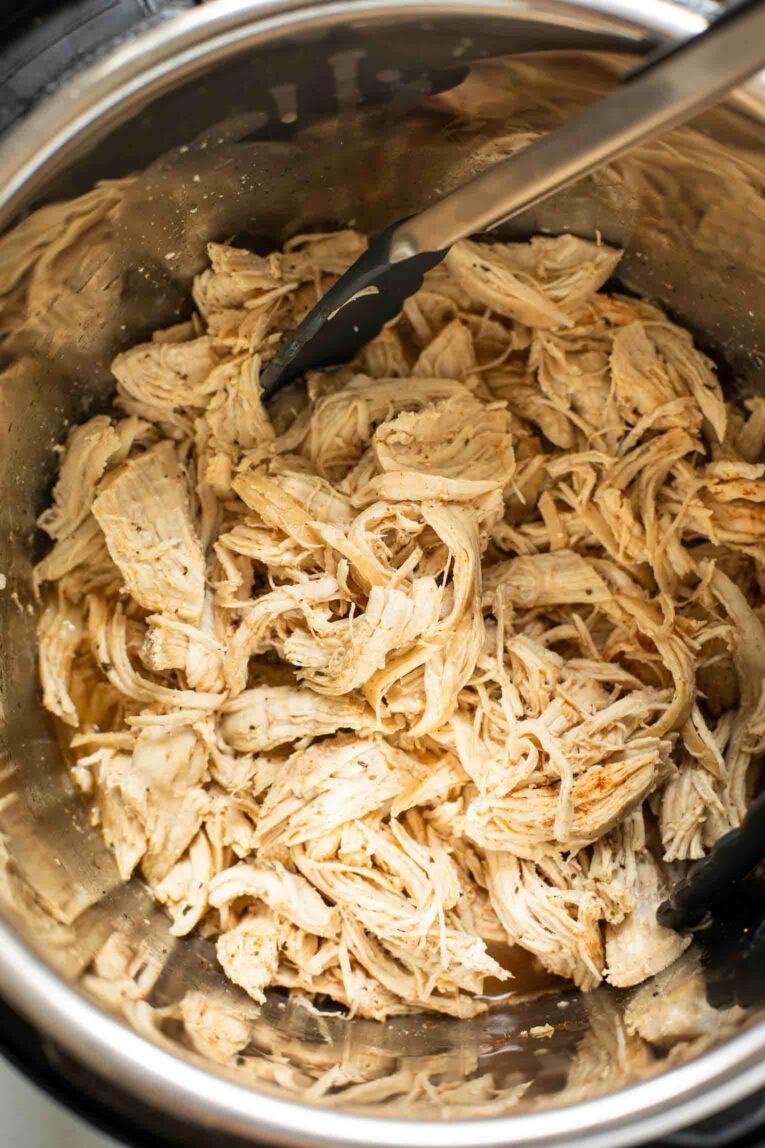 Top shot of tongs shredding chicken in an instant pot.