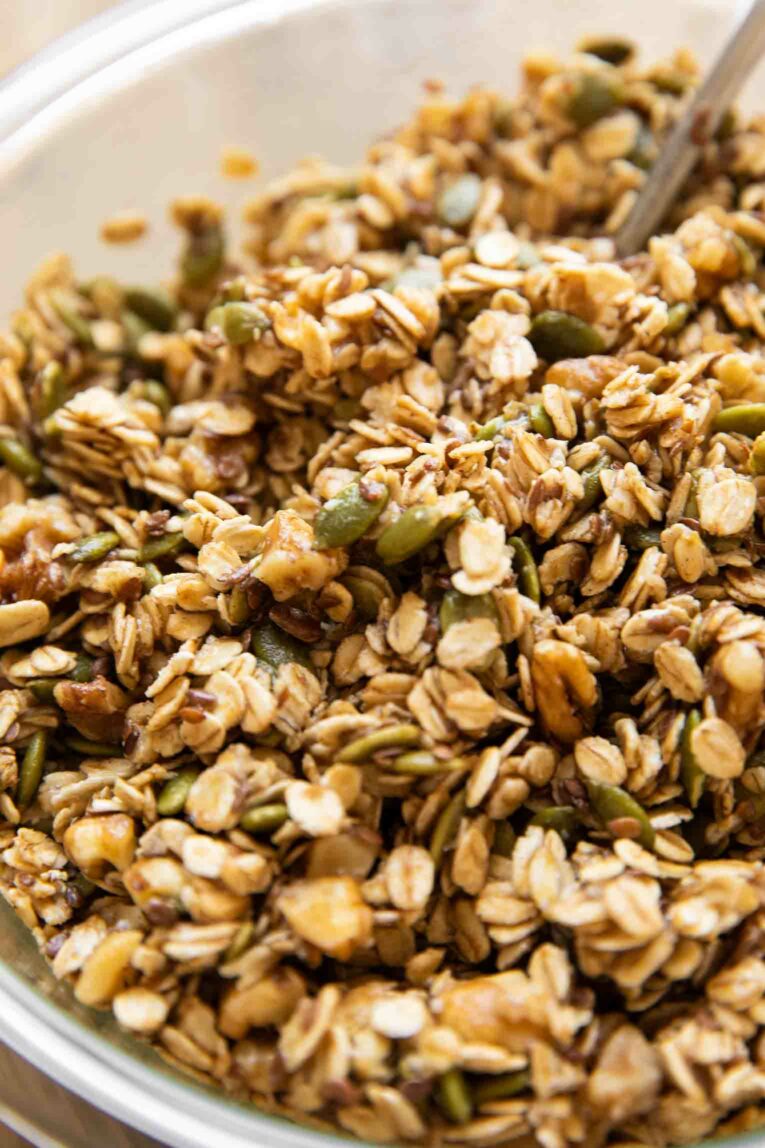 Ingredients for pumpkin flax granola being mixed in a glass bowl.